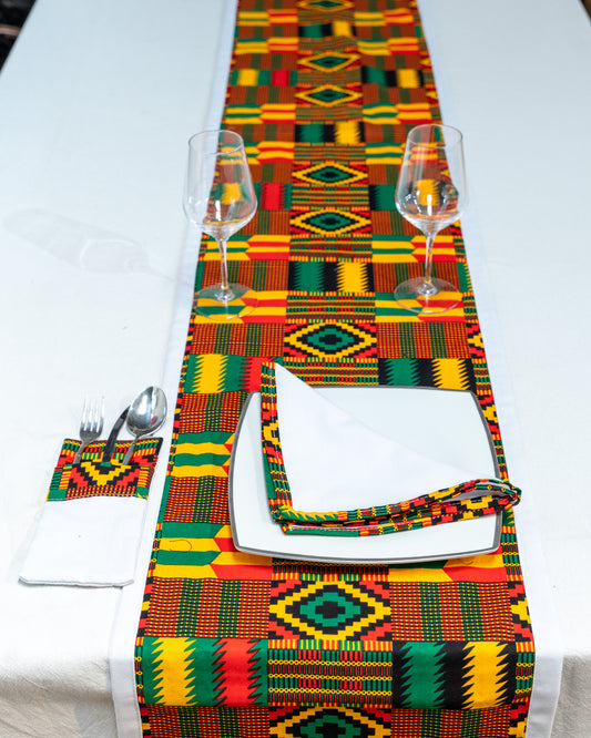 Colorful Kente cloth table runner with glasses, plates, and napkins on a white table.