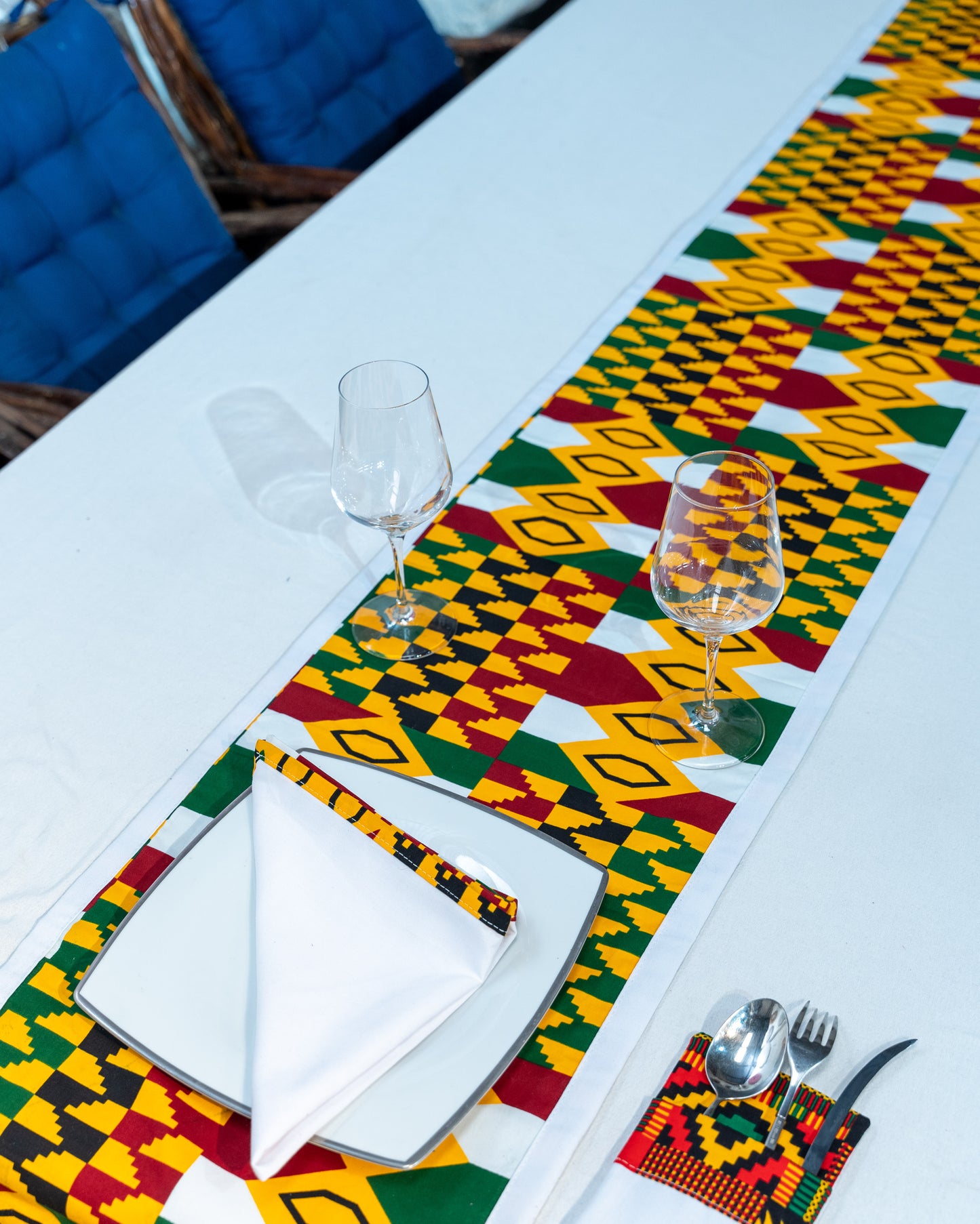 Dining table setting with a colorful patterned table runner, glasses, cutlery, and napkins.