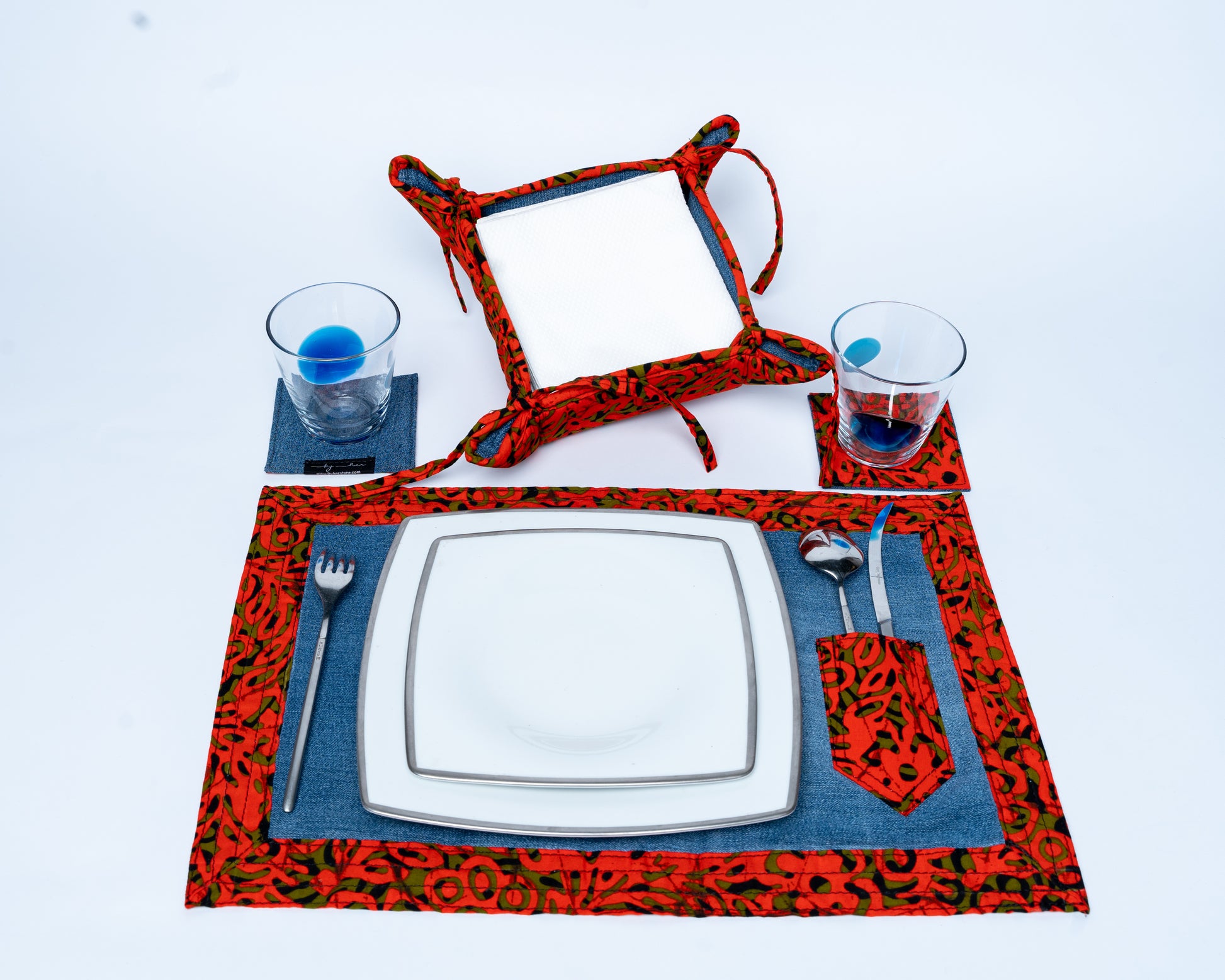 Table setting with red and black patterned placemats, glasses, and cutlery on a white background