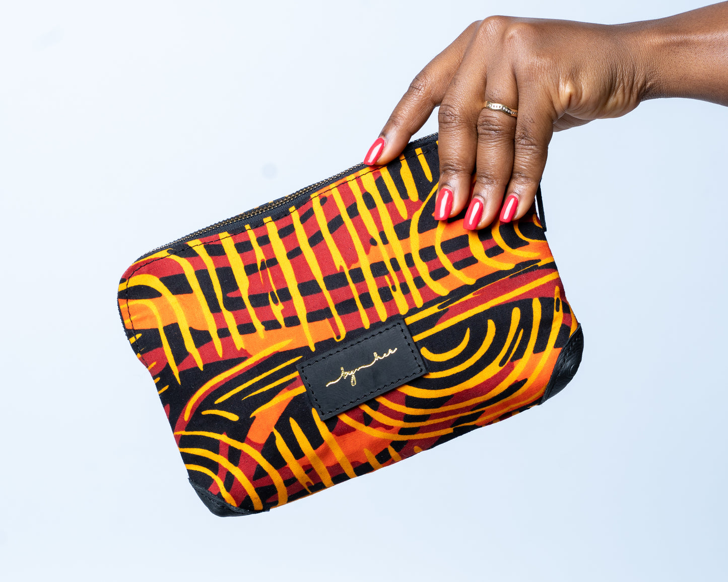Hand holding a colorful patterned clutch bag against a light gray background