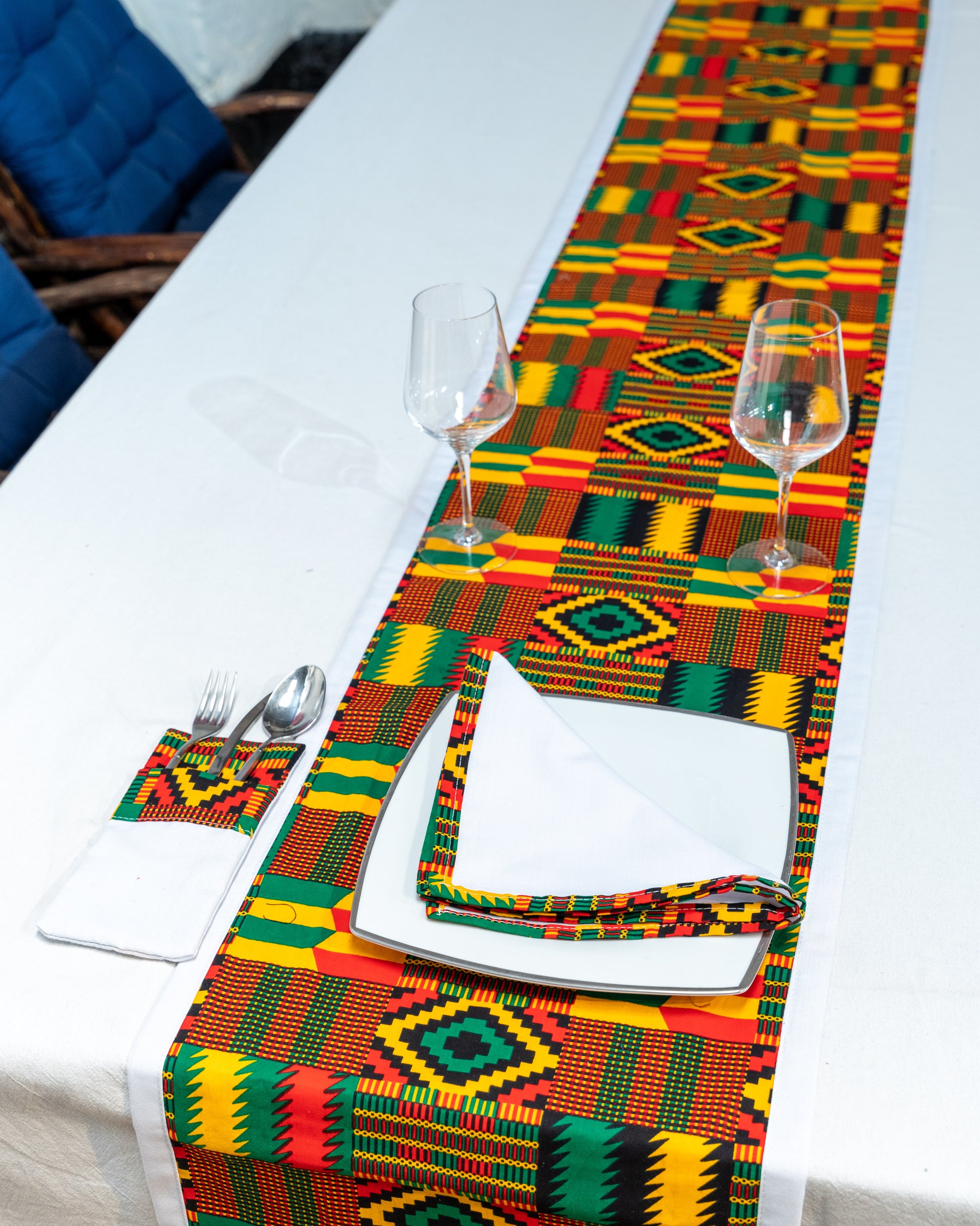 Colorful geometric-patterned table runner on a white table with cutlery and glasses.