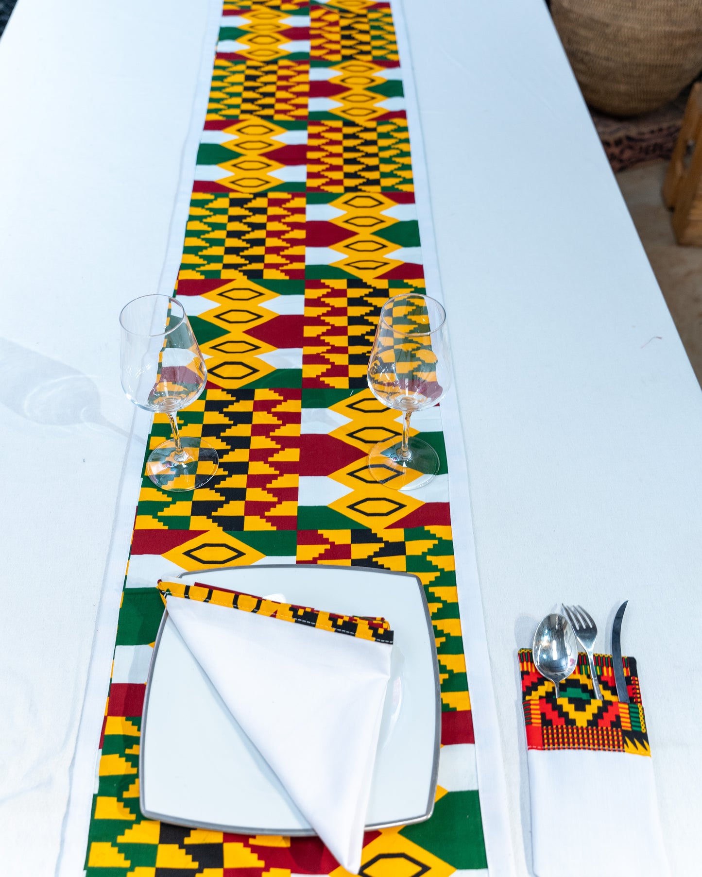 Colorful Kente pattern table runner on a white table with place settings.