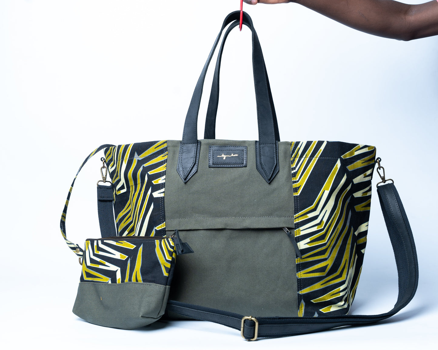 Green and yellow patterned bag with a matching pouch held by a person against a white background